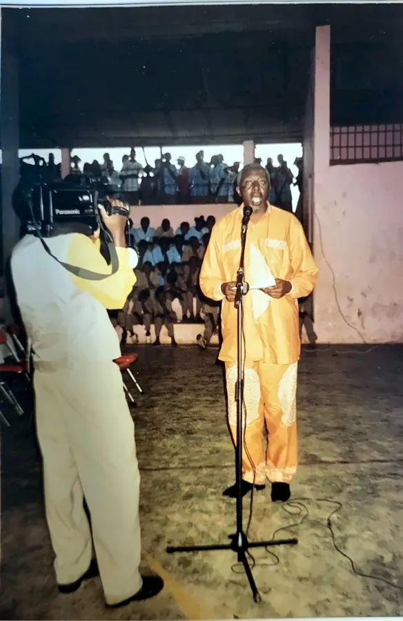 Paul Sanjong au micro, en tenue orange, devant des élèves